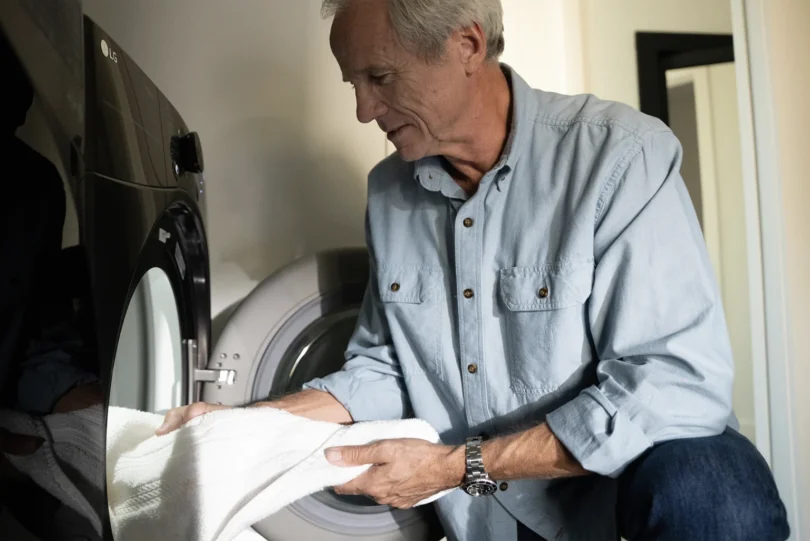 a man holding a white towel kneeling in front of a washing machine